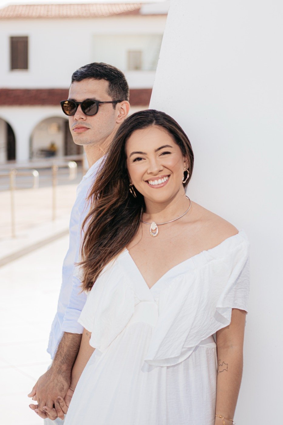 Casal sorrindo em frente a um prédio branco
